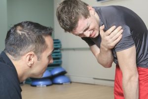 A man talking with another man whose holding his shoulder in pain