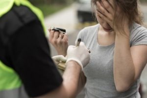 A person holding their head in one hand while a police officer stands in front of them and writes in a pad.