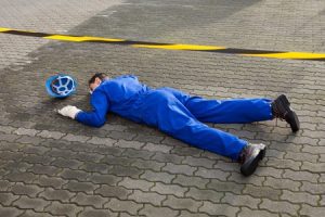 A man lying face down on the pavement after a slip, trip, or fall at work.