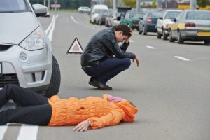 A distressed driver crouches next to an unconscious pedestrian who has been hurt in an accident