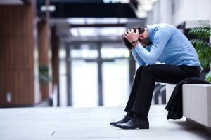 A person sat outside an office with their head bowed and held between their hands, with their elbows resting on their knees
