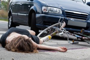 A cyclist knocked off their bike by a car lies on the road