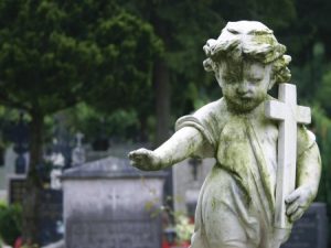 A statue of a child holding a cross in a graveyard.