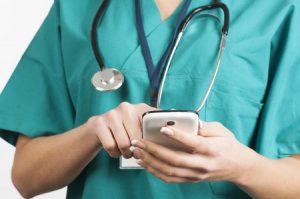 A doctor in green scrubs holding a mobile phone. 