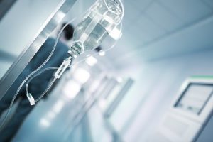 An out of focus hospital corridor with an IV equipment close up in the foreground. 