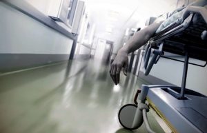 A hospital corridor with a gurney that has a patient's arm hanging over it. 