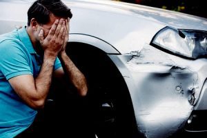 A man looking distressed next to a damaged car.