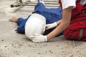 A worker lying unconscious on the ground being checked on by a colleague.