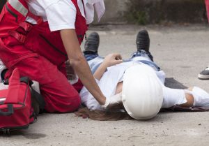 A woman lying on the floor after a lifting injury. Her colleague is helping her.