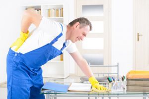 A man in work overalls holds his back. 