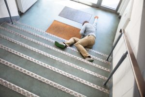 A man lying at the bottom of a flight of stairs following a slip and trip.