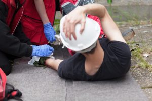 A worker on the floor wearing a white hard hat holding his head.