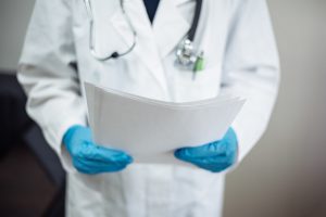 A doctor wearing blue latex gloves and holding some medical documents