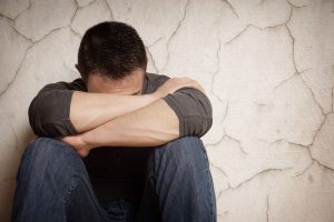 A man sat against a wall with his knees up and face pressed into his crossed arms