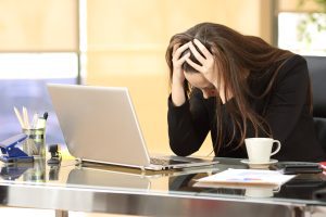 A visibly distressed woman with her head in her hands sat at a desk.