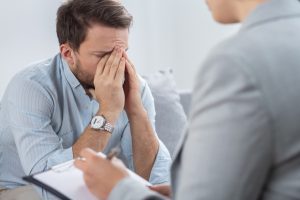 A man visibly distressed with his hands to his face talking to a psychologist