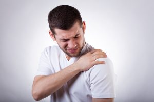 A man in a white t-shirt holds his shoulder in pain