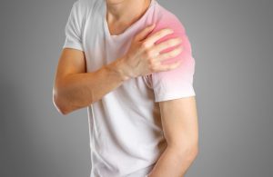A man in a white t-shirt puts his hand over a red area on his shoulder