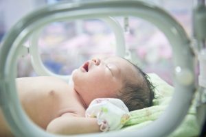 A baby cries on its back in an incubator