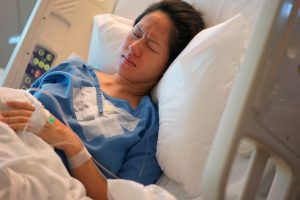 Female patient lying in the hospital bed frowning and in pain.