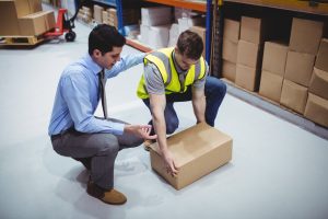 A man in a suit guides an employee in a high vis vest through a manual handling task