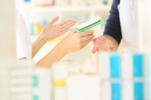 A pharmacist holding a white and green packet of medication and handing it to someone over the counter. 