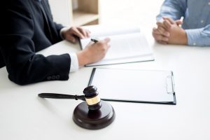 A solicitor in a dark suit writes in a file behind a black gavel