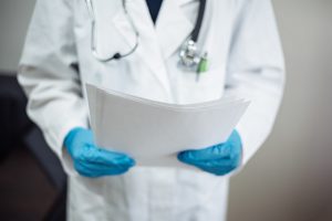 A doctor in a white coat and blue gloves holds a hospital chart