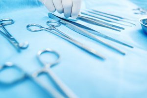 A white gloved hand reaches for a surgical instrument on a sterile tray