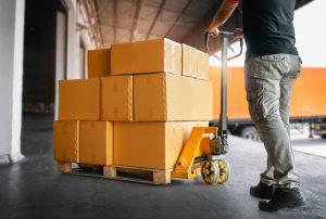 A person moving a pallet of boxes using a hand truck.