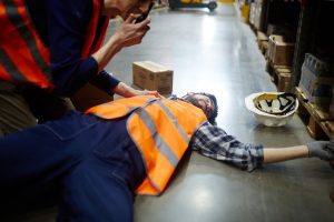 An employee calling for help and leaning over another employee who is lying on the floor unconscious after a slip and fall.