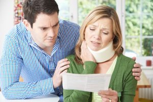 A husband and wife reading a letter about the wife's neck injury as she clutches at her neck collar.