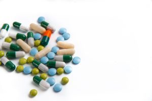 A pile of pills, all a variety of colours and shapes, with a white background. 