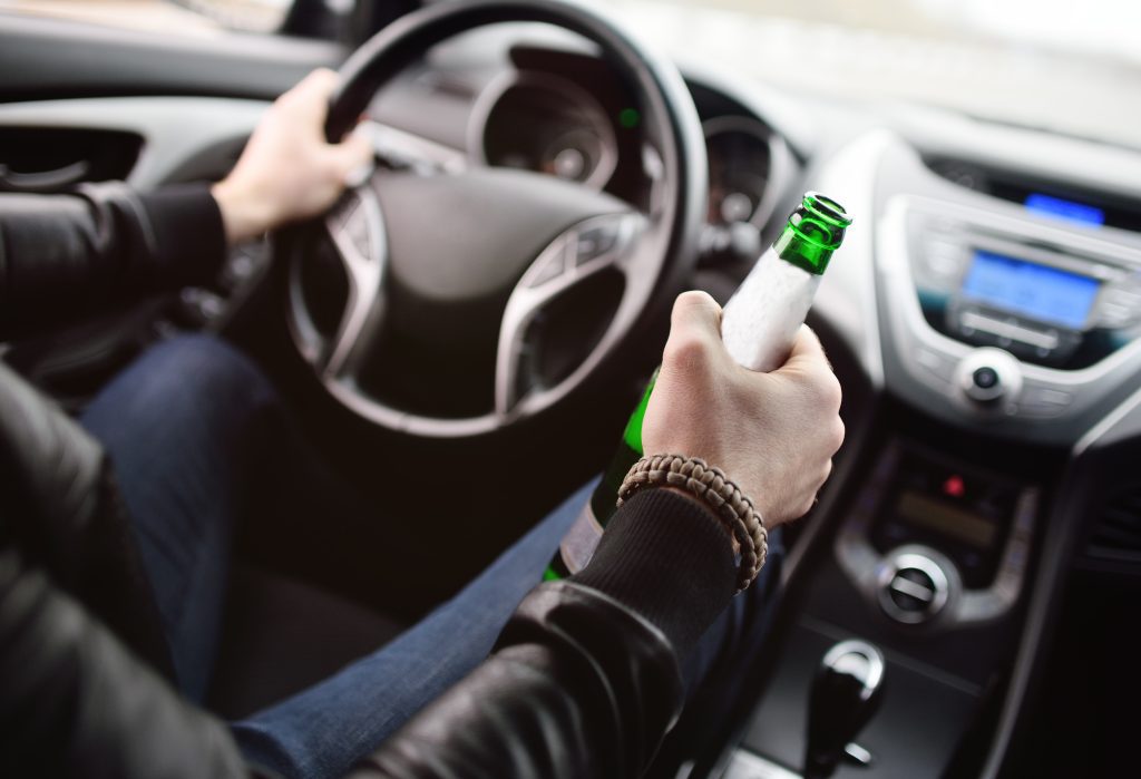 Drunk young man with a beard with a bottle of beer in his hand behind the wheel of a car. Emergency situation, violation of law, drunk driving