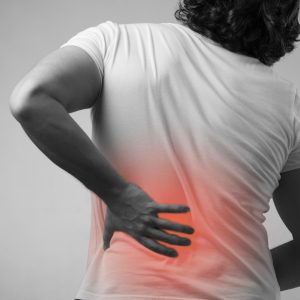 A man in a white T-shirt holds a hand to a red painful spot on his back