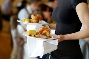 Torso shot of a waitress wearing a black t-shirt carrying a plate of food in each hand. 