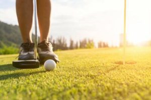 Golf player at the putting green hitting a ball