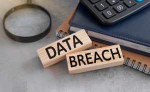 Two wooden blocks reading data breach sit on a desk beside notebooks and a magnifying glass