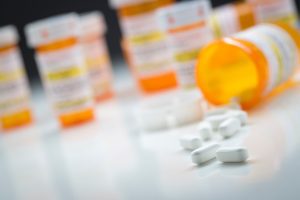 An orange pill bottle spills painkillers over a white table.
