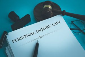 The words 'personal injury law' written on a white piece of paper on a blue table with a gavel, pair of glasses, a stamp and a pen next to the paper. 