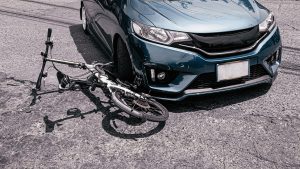 A bicycle underneath the driver's side wheel of a blue car on the road.