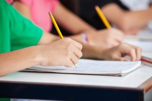 A close up of students writing on an exam paper while sitting at a desk