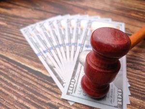 A red gavel on top of money notes spread out in a fan shape on a brown oak table to represent personal injury compensation.