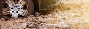A close up of car tires driving through mud.