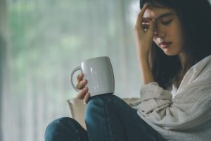 A woman sits by a window holding a mug while griving a close family member. She could be eligible to seek compensation through a financial dependency claim