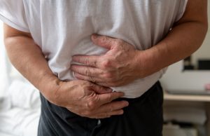 A man holds their stomach with both hands while suffering from food poisoning.
