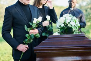Mourners wearing black and holding flowers gather a funeral service. A loved one's death can result in emotional difficulties and a financial burden