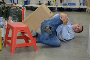 A man on the ground of a warehouse holding his knee after a workplace injury due to his employer's negligence