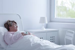 A woman lies down on her hospital bed and looks out of her room's window.