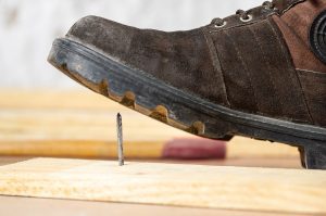 A man's boot steps over an exposed nail in a wooden plank.